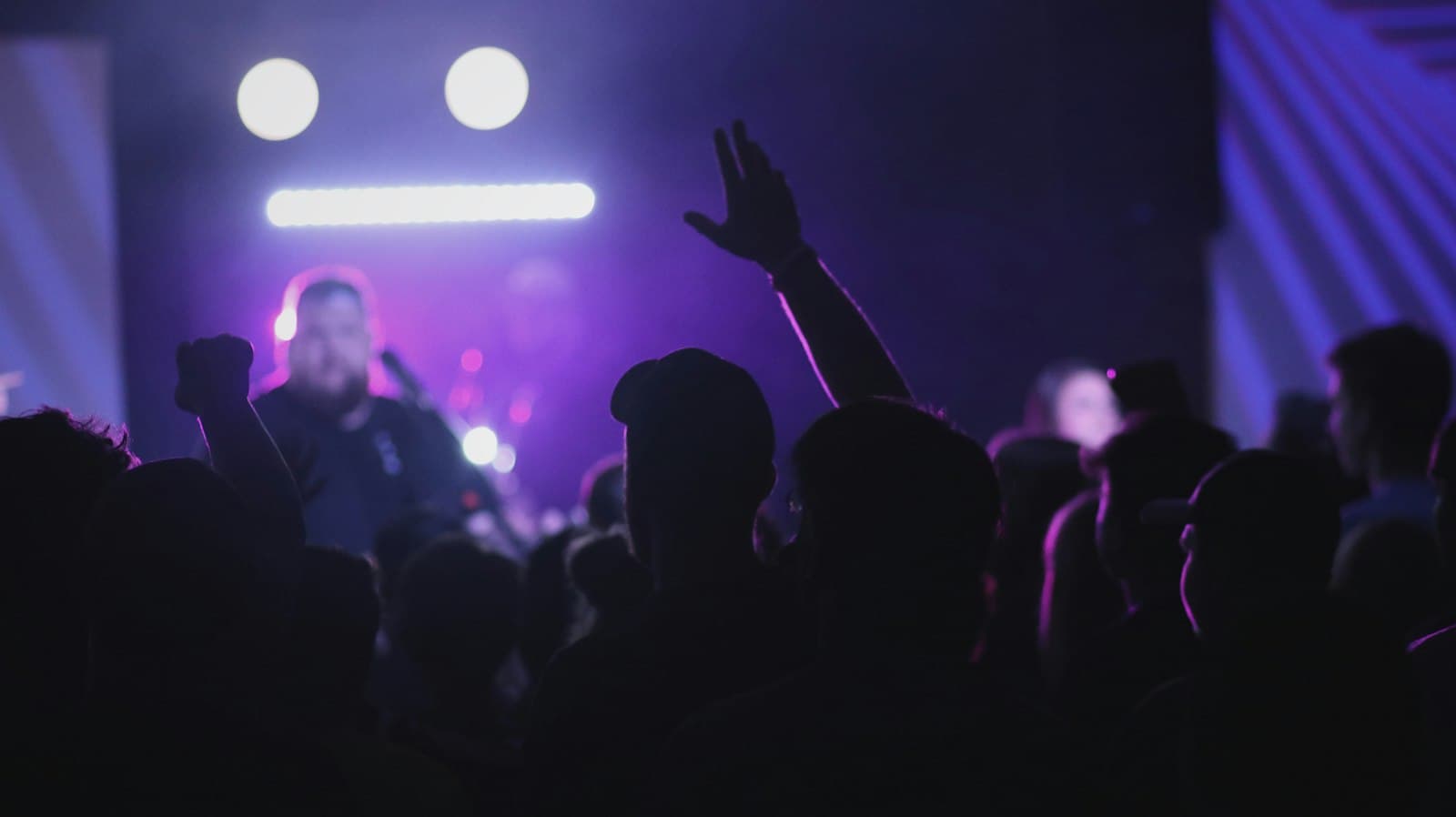 Público com as mãos para cima sob luzes roxas